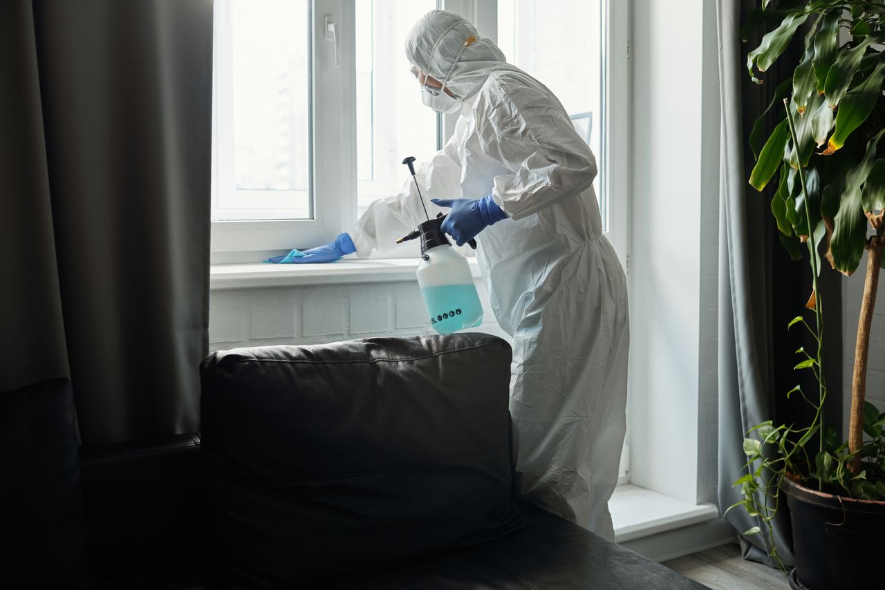 Person in PPE disinfecting indoor window area during COVID-19 pandemic.